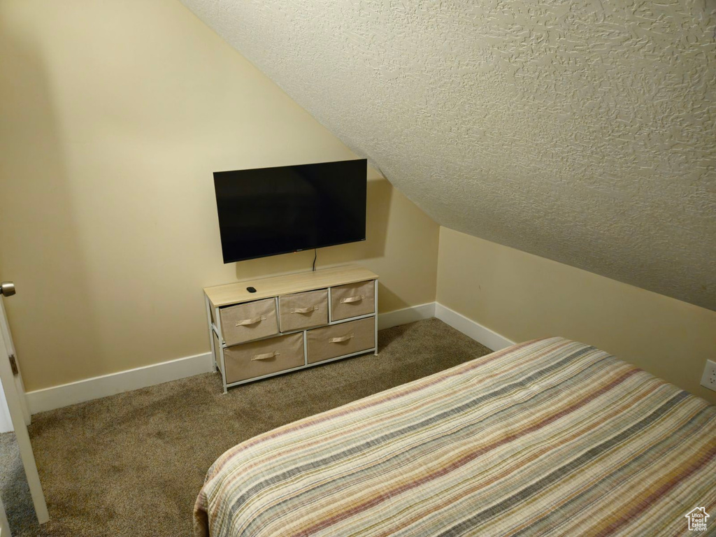 Bedroom featuring dark colored carpet, a textured ceiling, and lofted ceiling