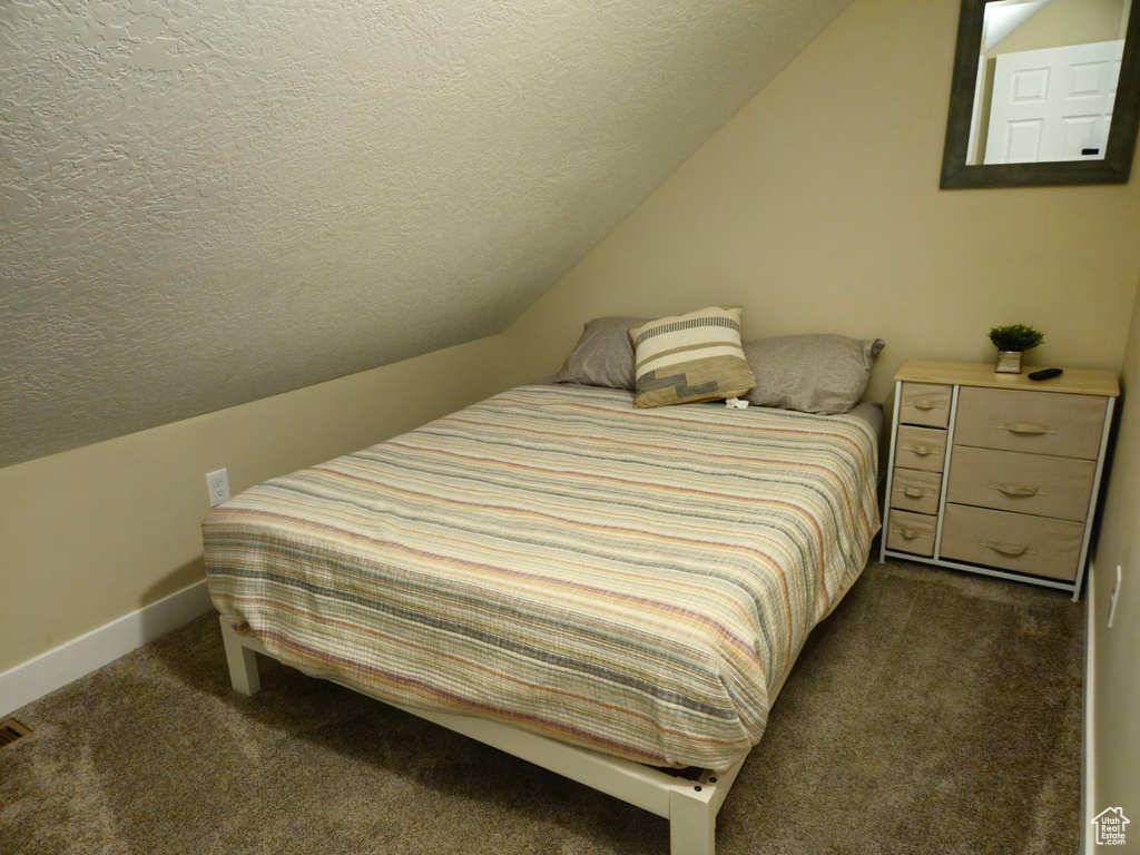 Bedroom featuring lofted ceiling, dark carpet, and a textured ceiling