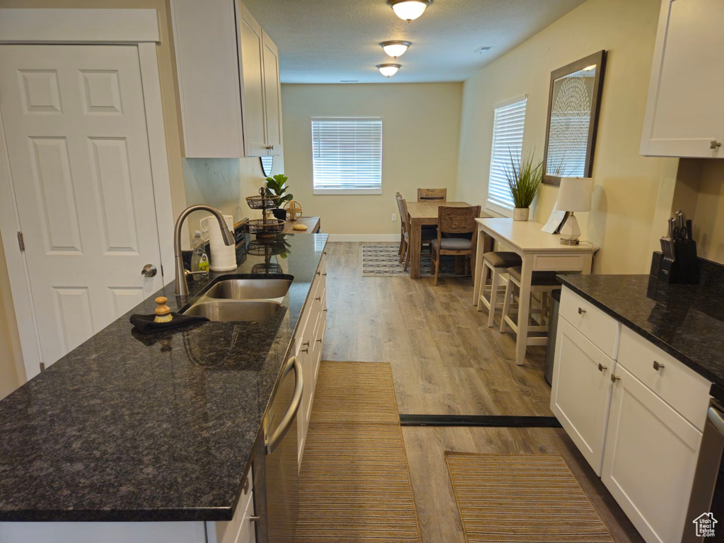 Kitchen with dark stone counters, white cabinetry, light wood-type flooring, and a kitchen island with sink