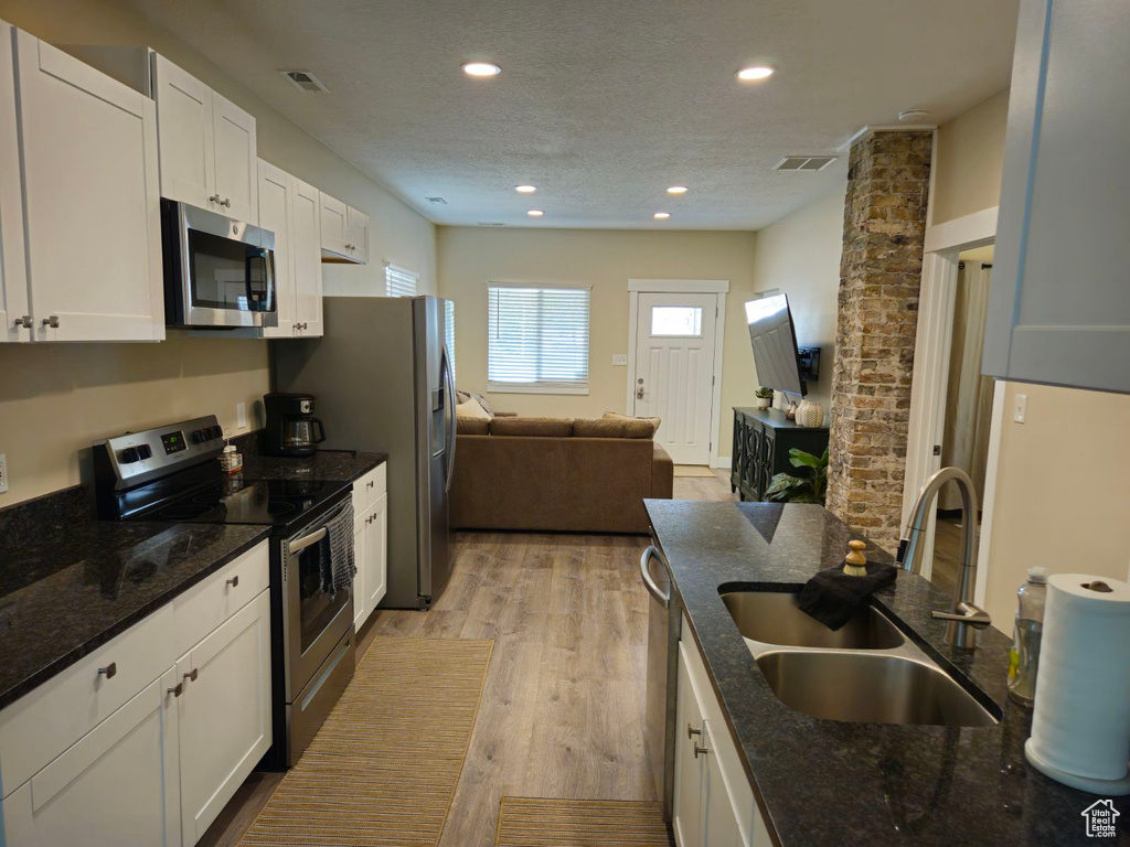 Kitchen with white cabinetry, dark stone countertops, light wood-type flooring, appliances with stainless steel finishes, and sink