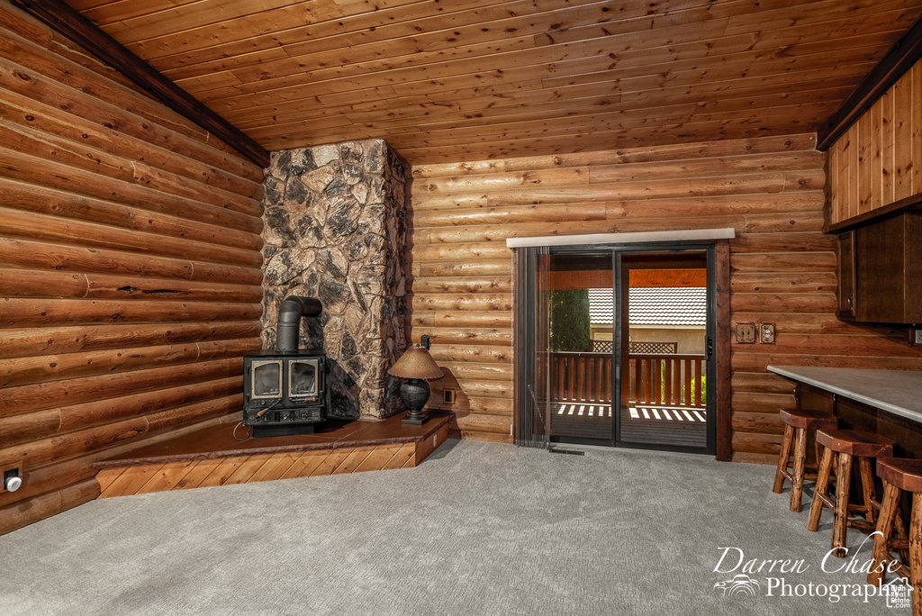 Unfurnished living room featuring a wood stove, carpet flooring, wooden ceiling, and log walls