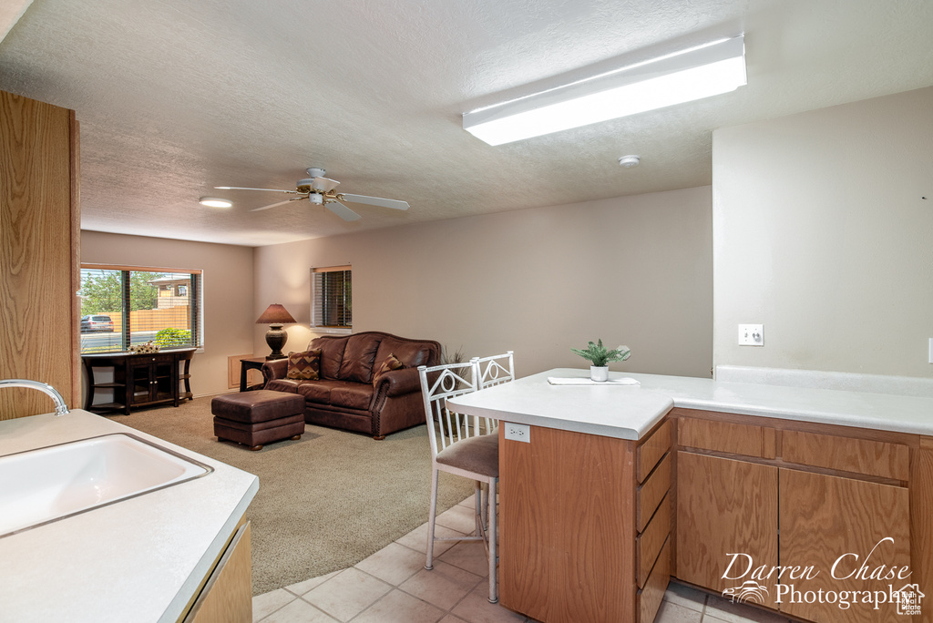 Kitchen with light tile patterned flooring, ceiling fan, sink, a breakfast bar, and kitchen peninsula