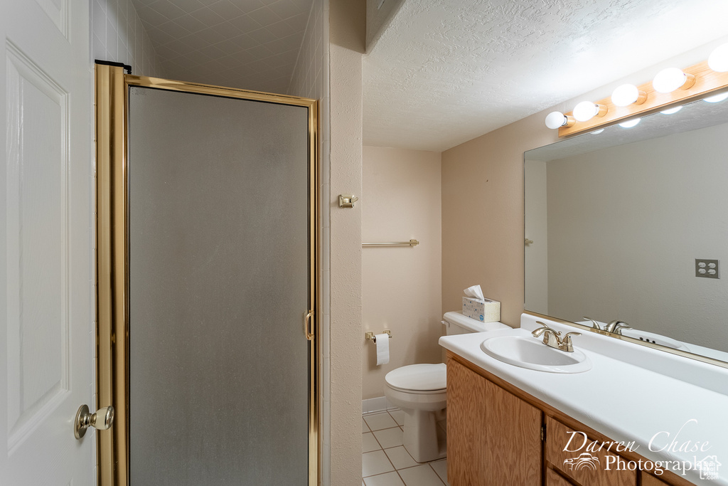 Bathroom with vanity, walk in shower, toilet, a textured ceiling, and tile patterned flooring