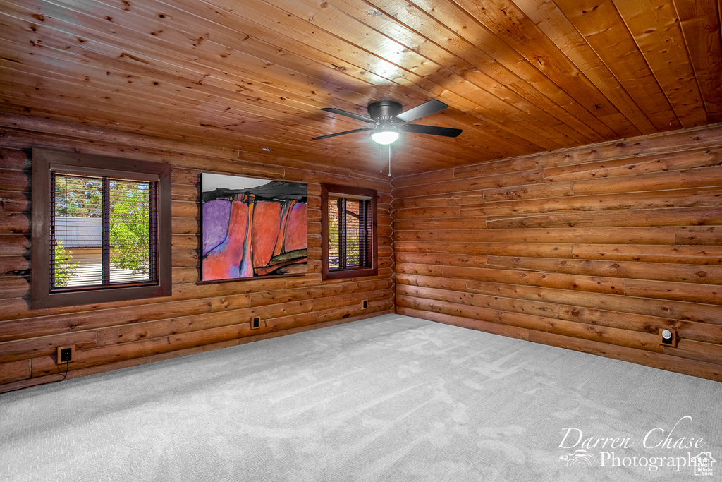 Carpeted spare room with ceiling fan, rustic walls, and wood ceiling