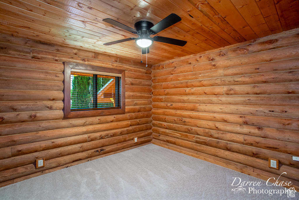 Empty room featuring ceiling fan, rustic walls, carpet floors, and wooden ceiling