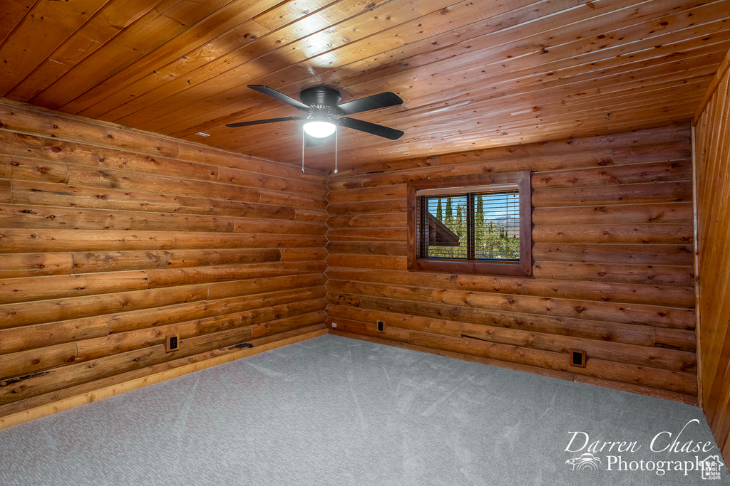 Carpeted spare room featuring wooden ceiling, ceiling fan, and log walls