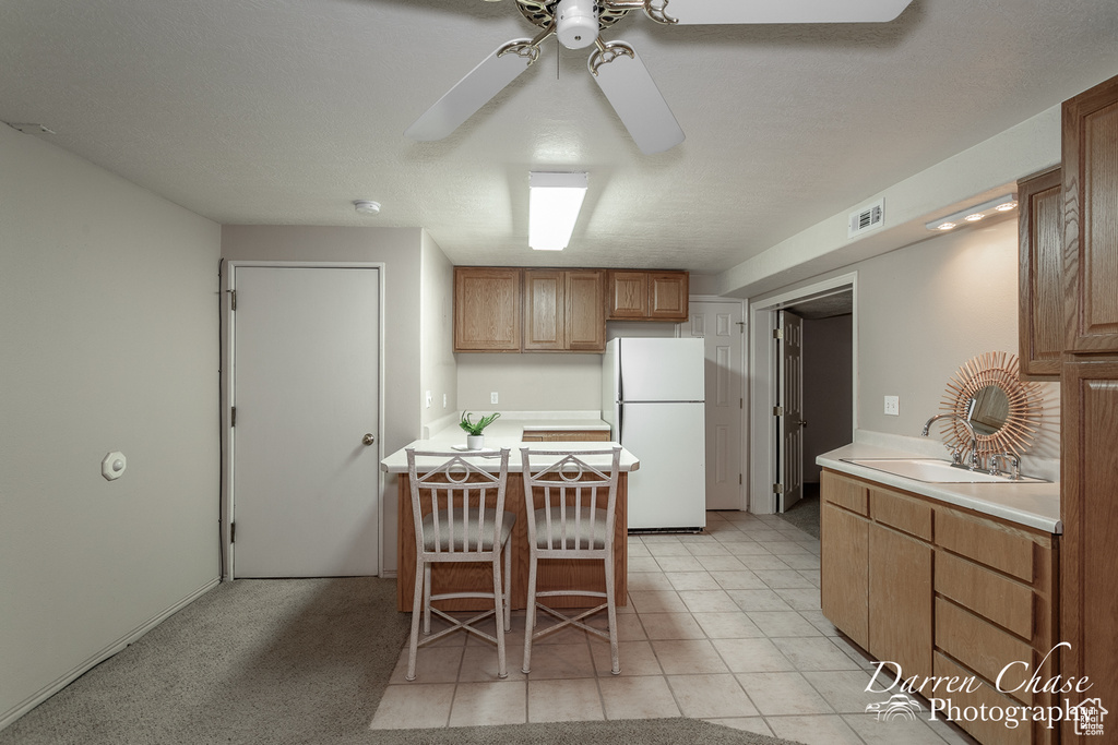 Kitchen with white refrigerator, a breakfast bar, sink, light tile patterned flooring, and ceiling fan