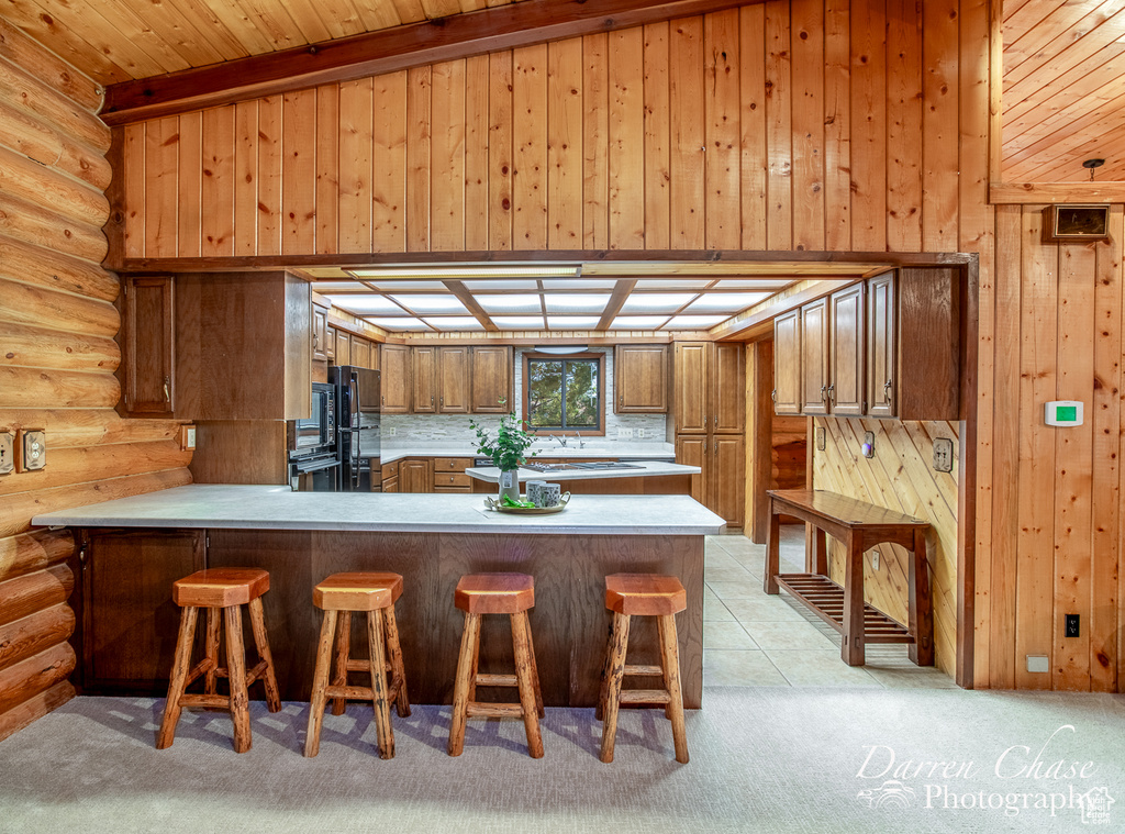 Kitchen with kitchen peninsula, black appliances, wooden ceiling, light carpet, and lofted ceiling with beams