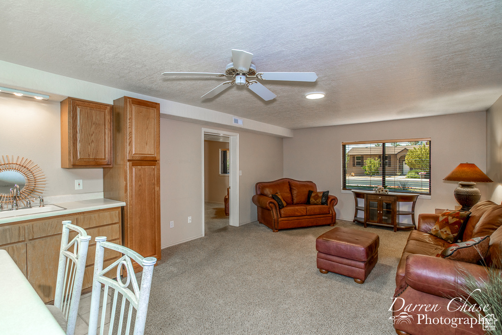 Living room featuring a textured ceiling, ceiling fan, and light colored carpet