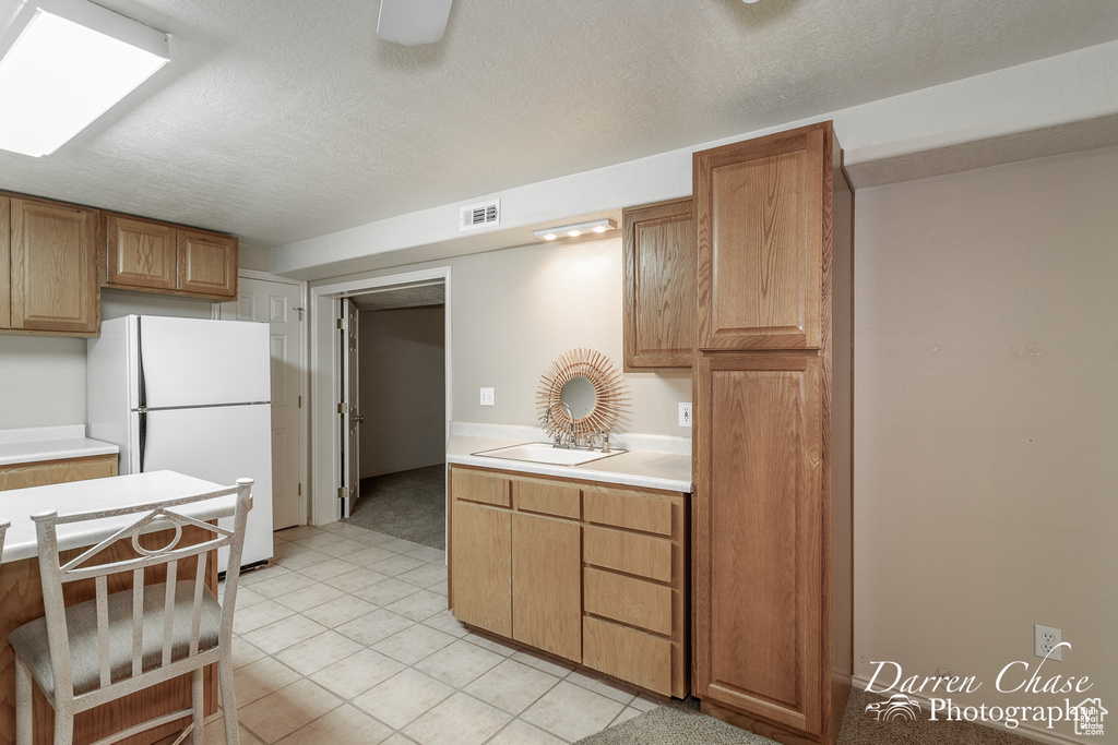 Kitchen with sink, light tile patterned floors, a textured ceiling, white fridge, and ceiling fan