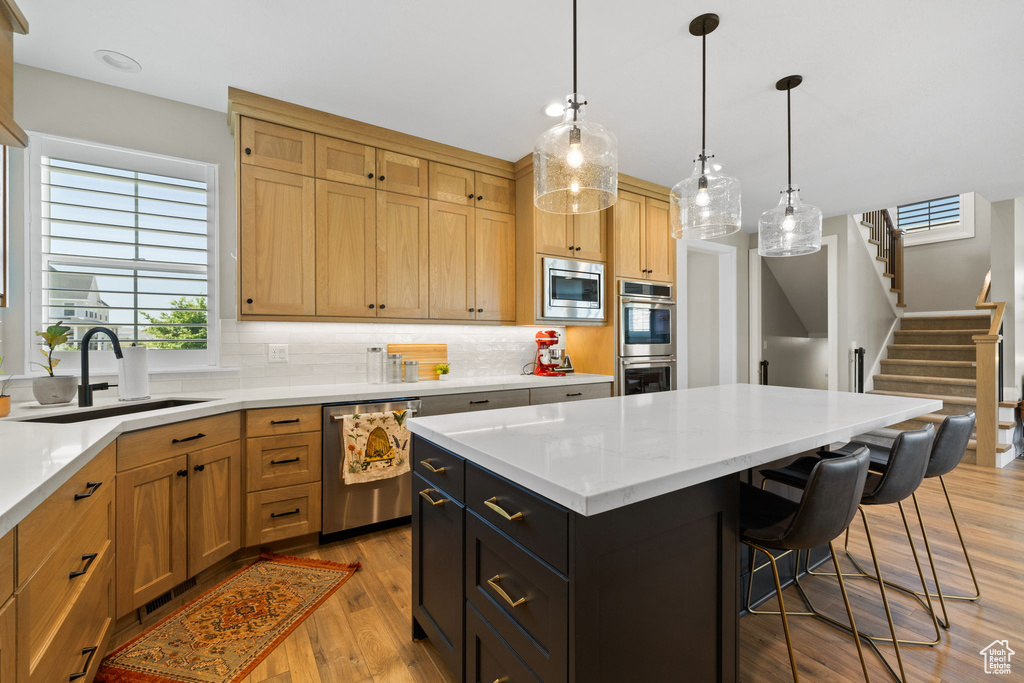 Kitchen featuring tasteful backsplash, stainless steel appliances, sink, pendant lighting, and light hardwood / wood-style floors