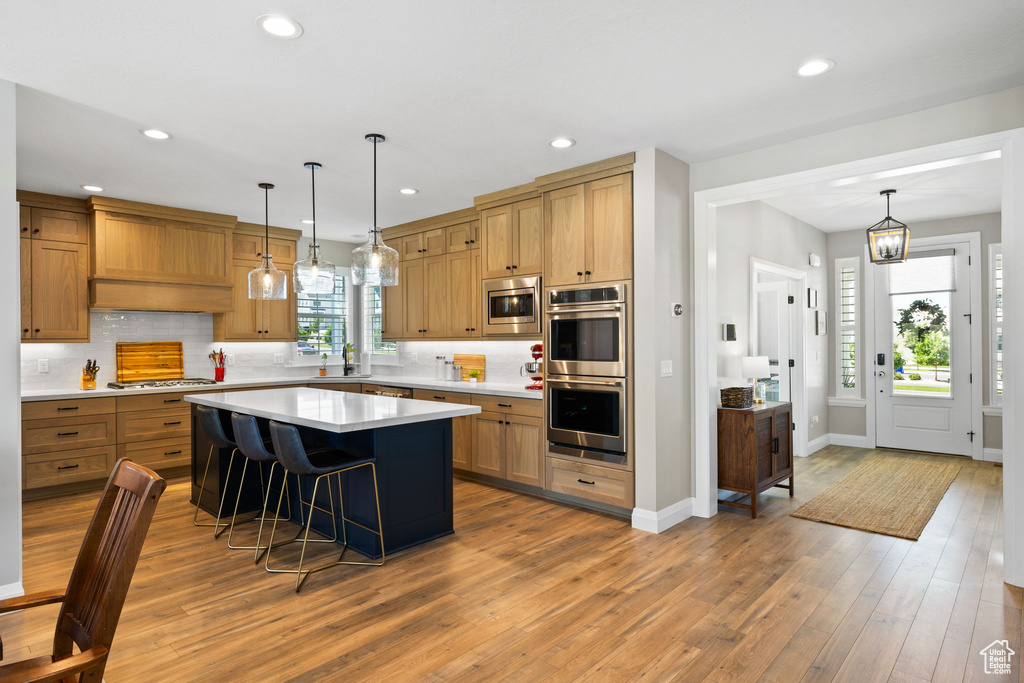 Kitchen featuring a center island, wood-type flooring, stainless steel appliances, and decorative light fixtures