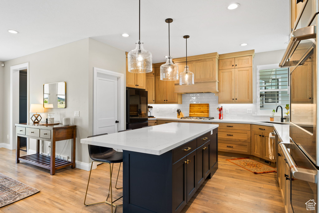 Kitchen with tasteful backsplash, hanging light fixtures, sink, a kitchen island, and light hardwood / wood-style floors