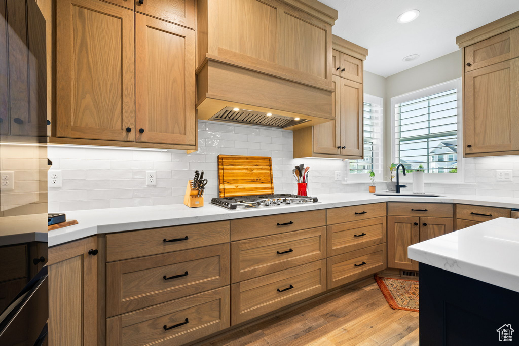 Kitchen with stainless steel gas stovetop, sink, decorative backsplash, light wood-type flooring, and custom range hood