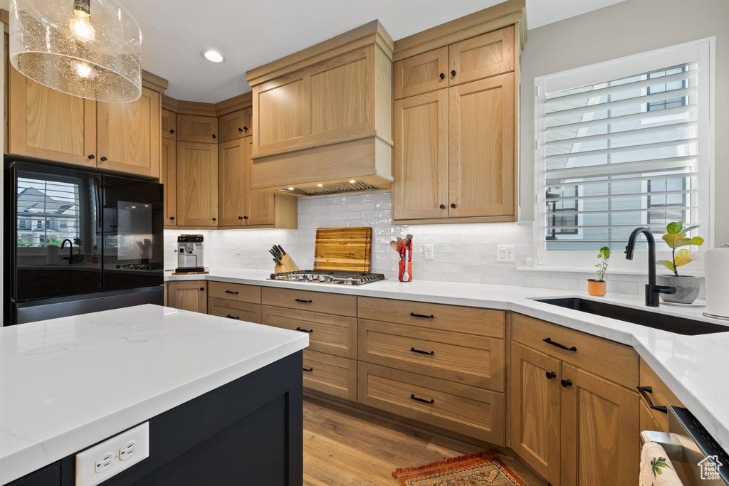 Kitchen featuring sink, custom range hood, appliances with stainless steel finishes, light hardwood / wood-style flooring, and backsplash