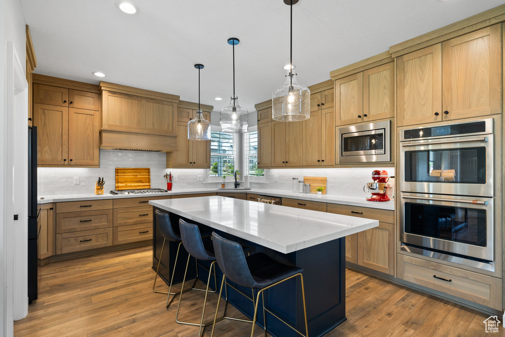 Kitchen with stainless steel appliances, hardwood / wood-style floors, a center island, custom range hood, and backsplash