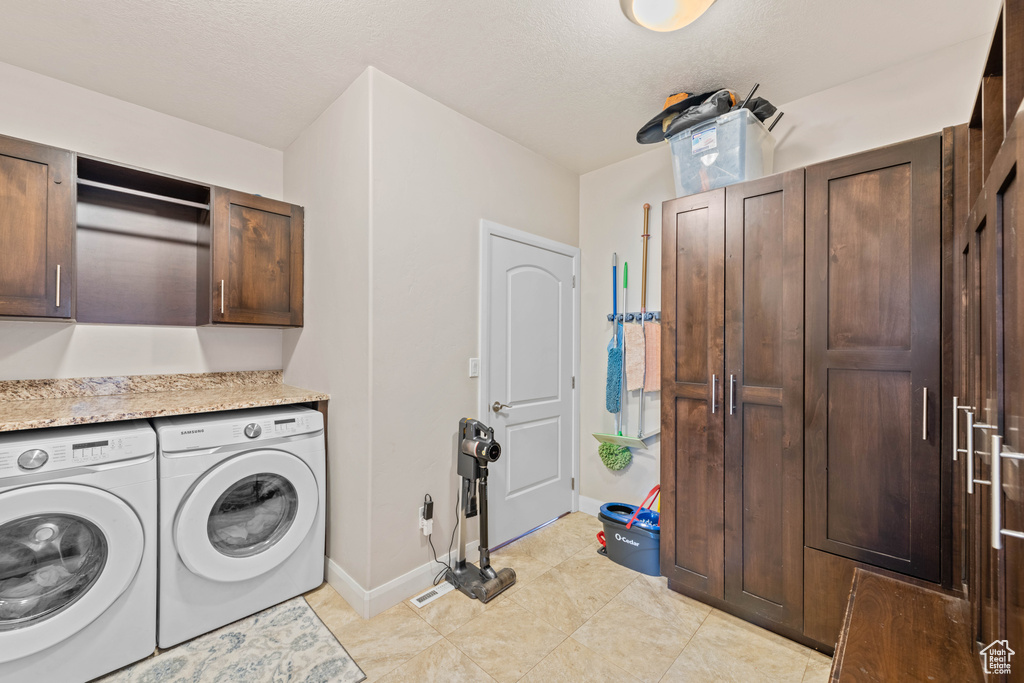 Clothes washing area with light tile patterned flooring, washing machine and clothes dryer, and cabinets