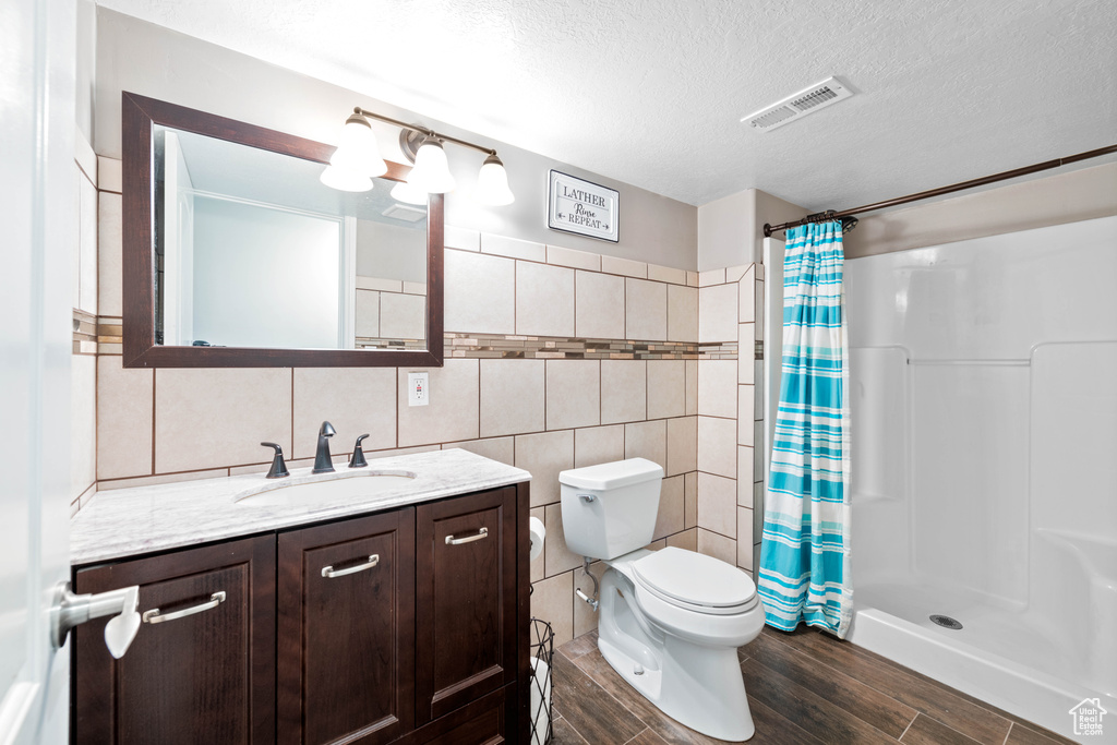 Bathroom with tile walls, walk in shower, a textured ceiling, toilet, and vanity