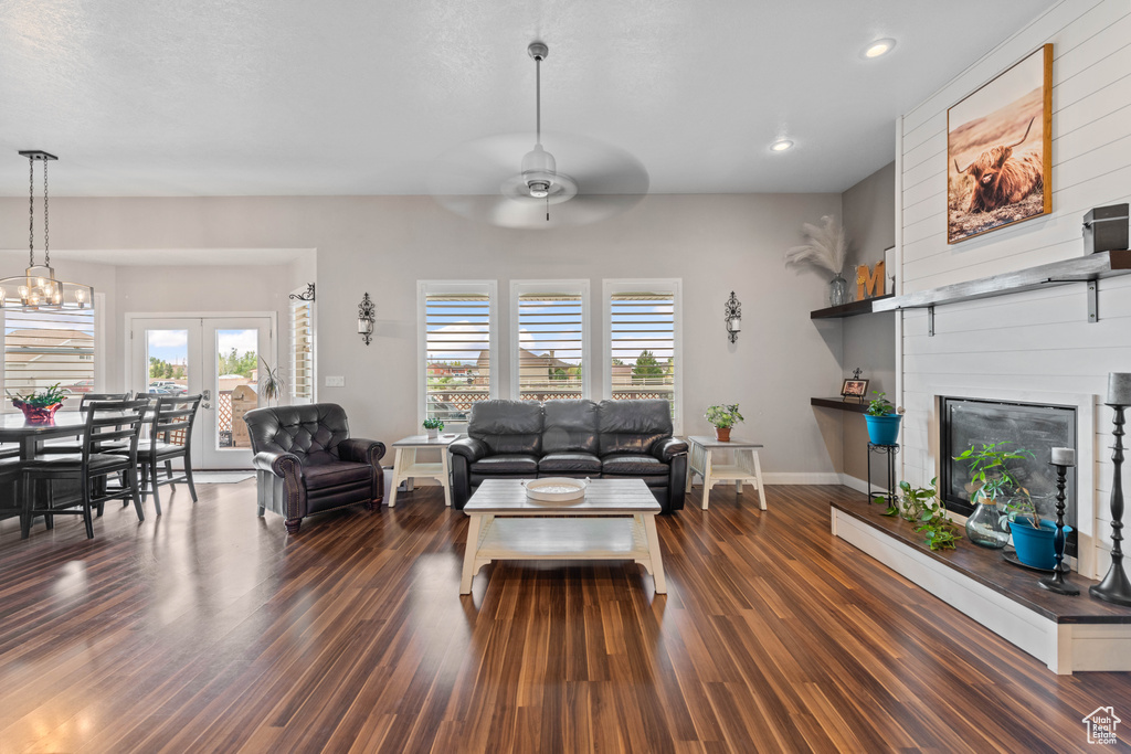 Living room with dark wood-type flooring, ceiling fan with notable chandelier, and a large fireplace