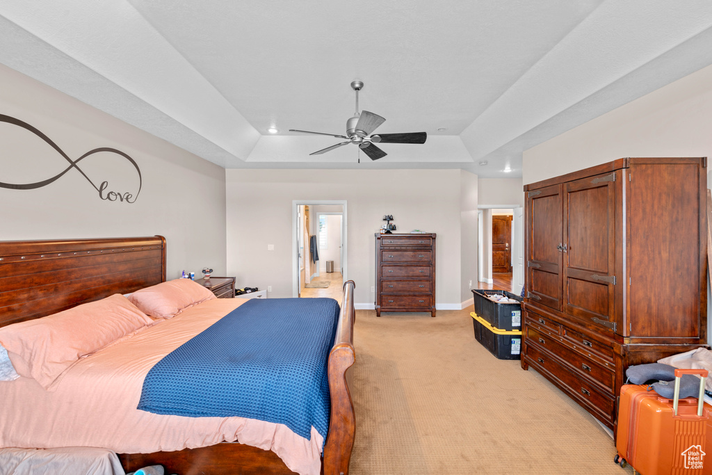 Bedroom with ceiling fan, a tray ceiling, connected bathroom, and light colored carpet