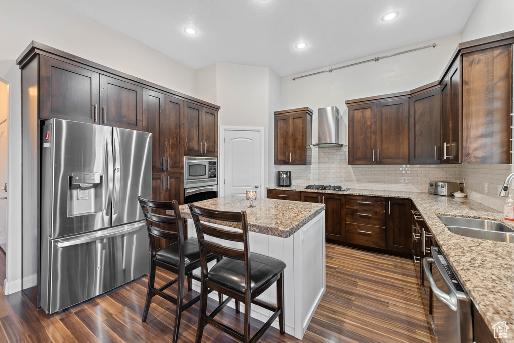 Kitchen featuring stainless steel appliances, decorative backsplash, wall chimney exhaust hood, a center island, and dark hardwood / wood-style floors