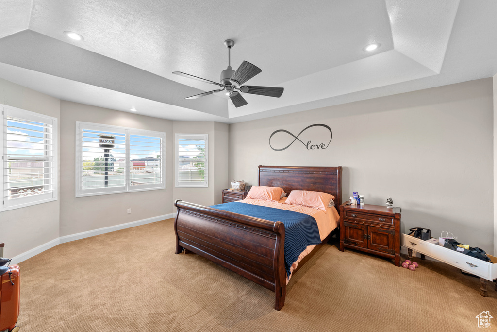 Carpeted bedroom featuring ceiling fan and a tray ceiling