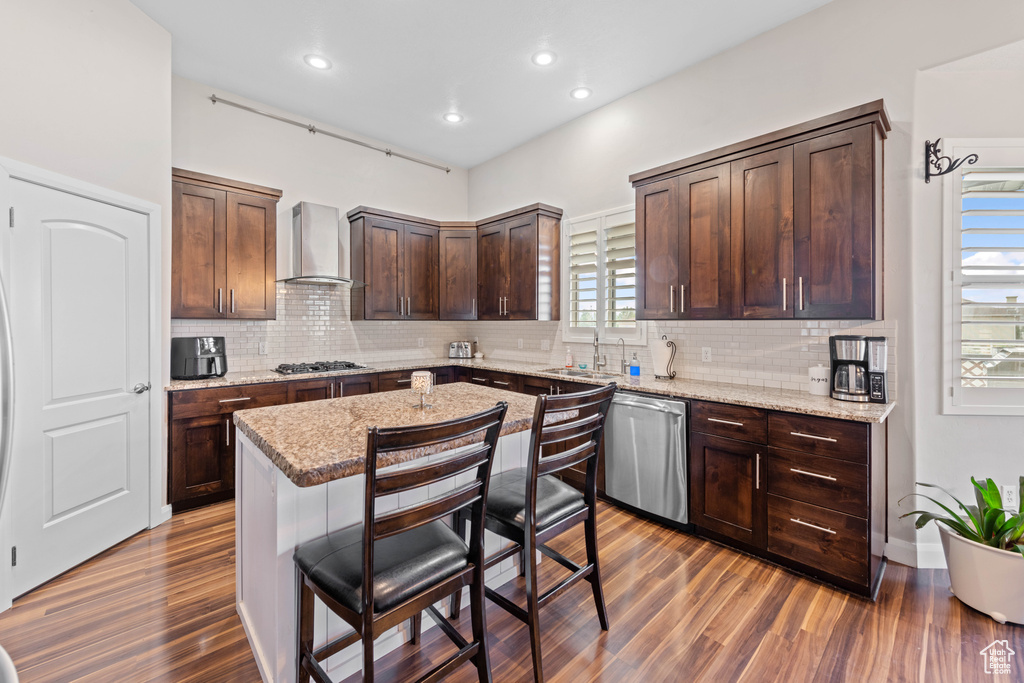 Kitchen featuring appliances with stainless steel finishes, dark hardwood / wood-style floors, tasteful backsplash, and wall chimney exhaust hood