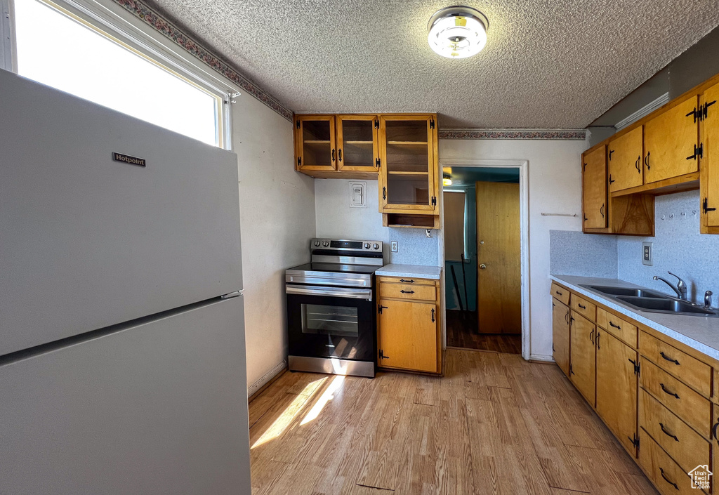 Kitchen with electric stove, luxury refrigerator, light hardwood / wood-style flooring, sink, and a textured ceiling