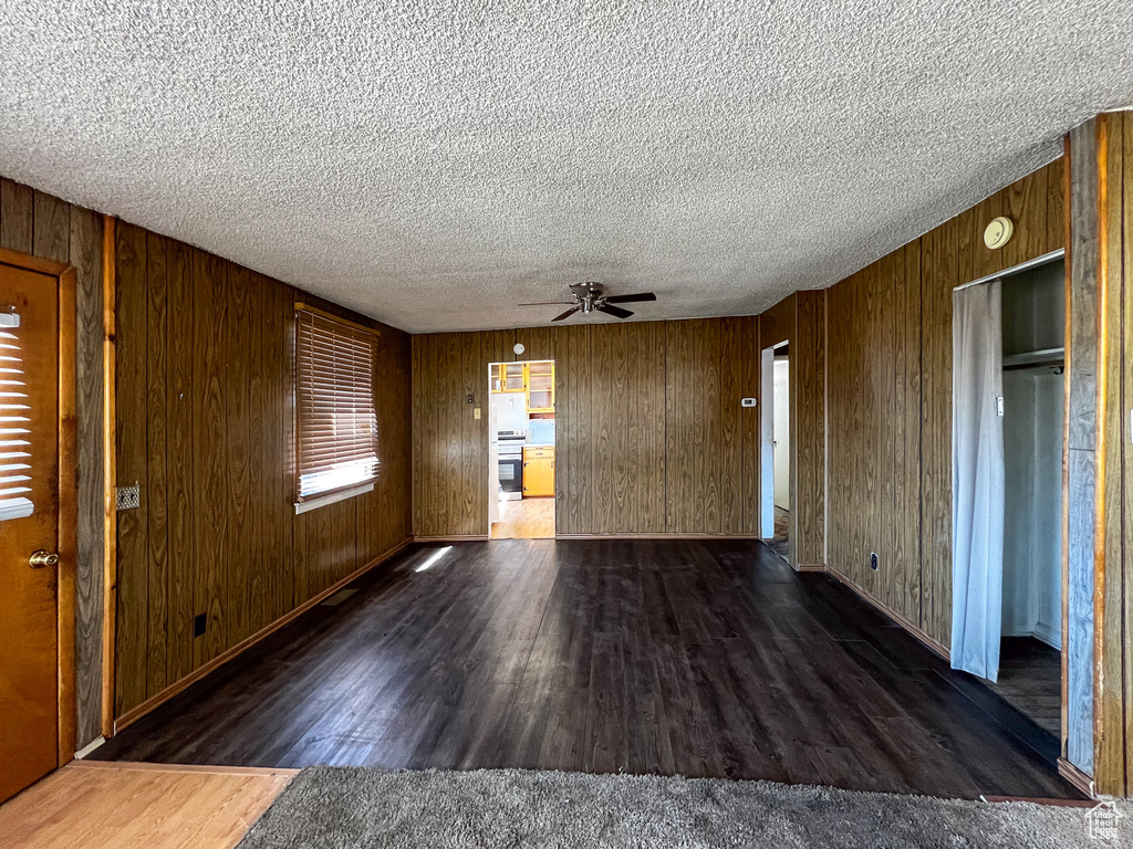 Unfurnished room featuring wood walls, a textured ceiling, and dark wood-type flooring