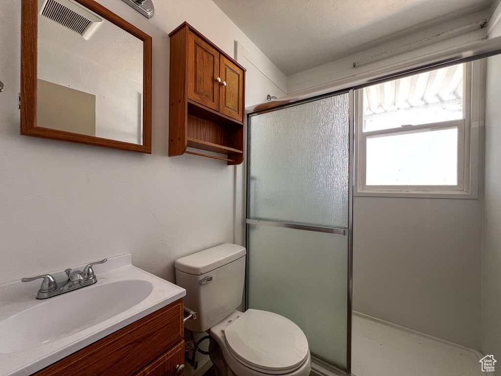 Bathroom with a shower with shower door, vanity, and toilet