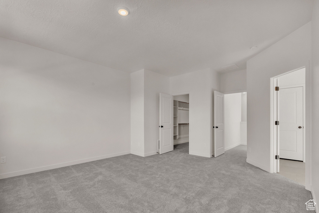 Unfurnished bedroom with light colored carpet, a textured ceiling, a closet, and a spacious closet