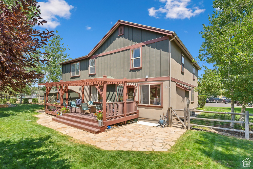 Rear view of property featuring a pergola, a patio area, a wooden deck, and a lawn