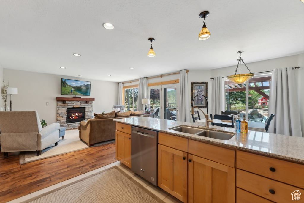 Kitchen with sink, dishwasher, light stone countertops, light hardwood / wood-style floors, and a stone fireplace