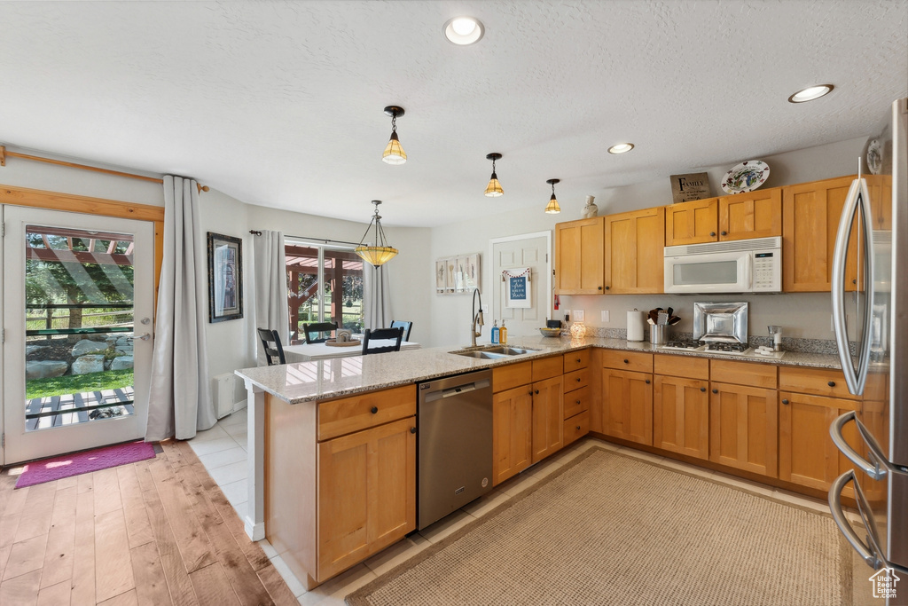 Kitchen with stainless steel appliances, sink, kitchen peninsula, light hardwood / wood-style floors, and decorative light fixtures