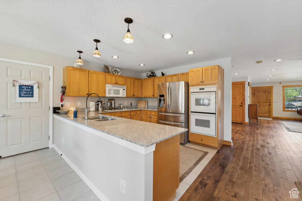 Kitchen featuring pendant lighting, white appliances, sink, light hardwood / wood-style floors, and kitchen peninsula