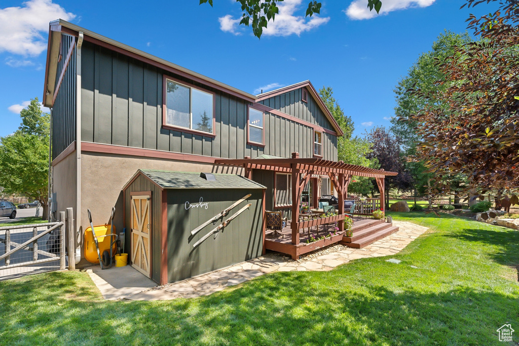 Back of property with a wooden deck, a lawn, a shed, and a pergola