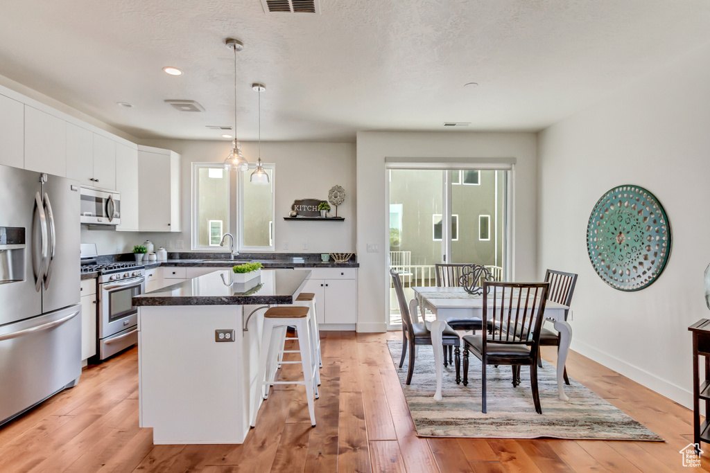 Kitchen with white cabinetry, light wood-type flooring, hanging light fixtures, appliances with stainless steel finishes, and a kitchen breakfast bar