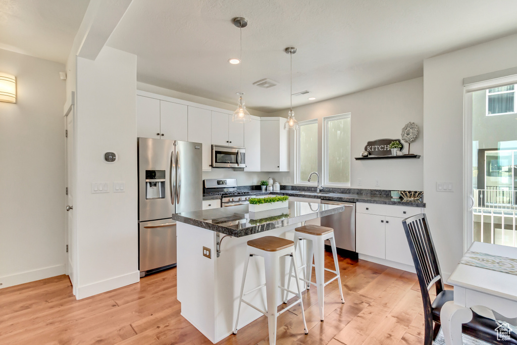 Kitchen featuring appliances with stainless steel finishes, hanging light fixtures, light hardwood / wood-style floors, a center island, and white cabinetry