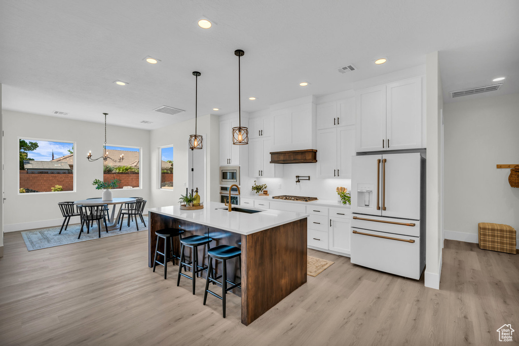 Kitchen featuring appliances with stainless steel finishes, white cabinets, a center island with sink, and light wood-type flooring