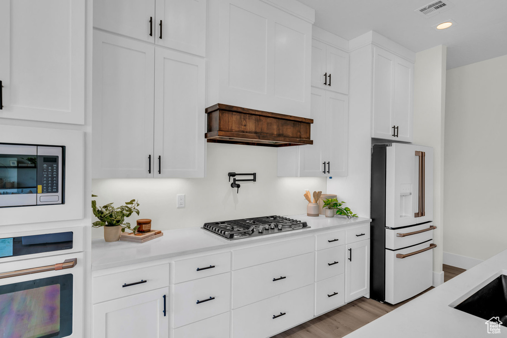 Kitchen featuring appliances with stainless steel finishes, light hardwood / wood-style flooring, white cabinets, and custom exhaust hood