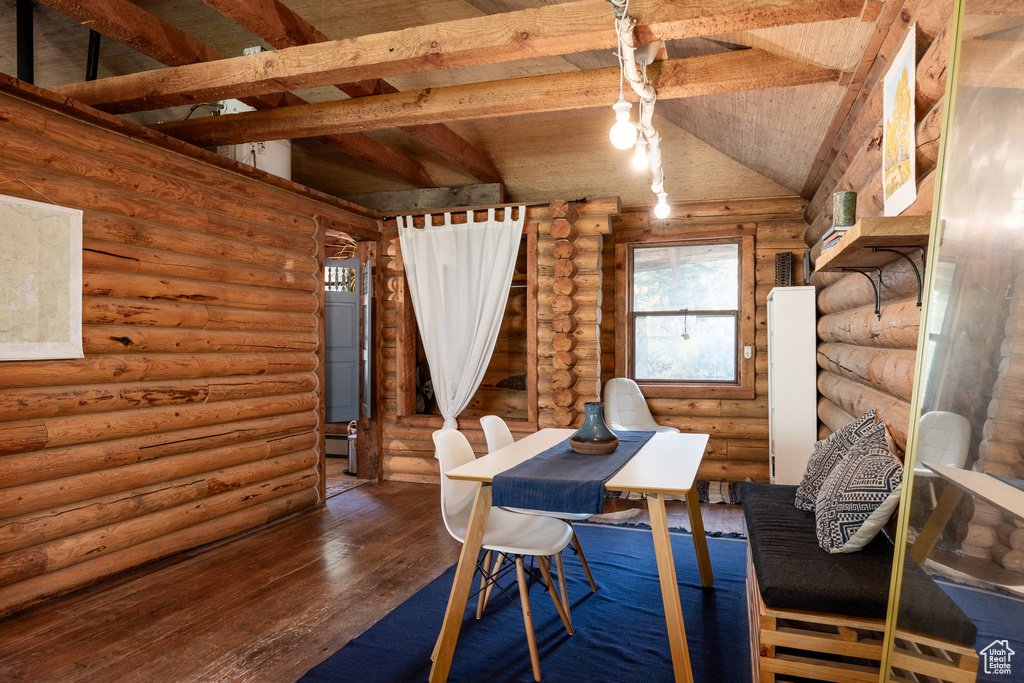 Unfurnished dining area featuring vaulted ceiling with beams, hardwood / wood-style flooring, and rustic walls