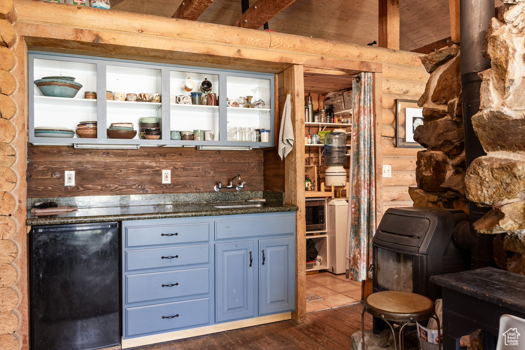 Bar with dark stone countertops, rustic walls, fridge, hardwood / wood-style floors, and sink