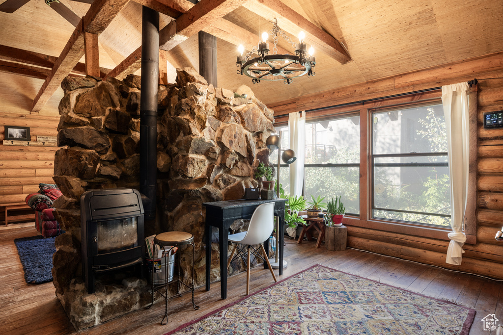 Interior space with a notable chandelier, wood-type flooring, a wood stove, rustic walls, and lofted ceiling with beams