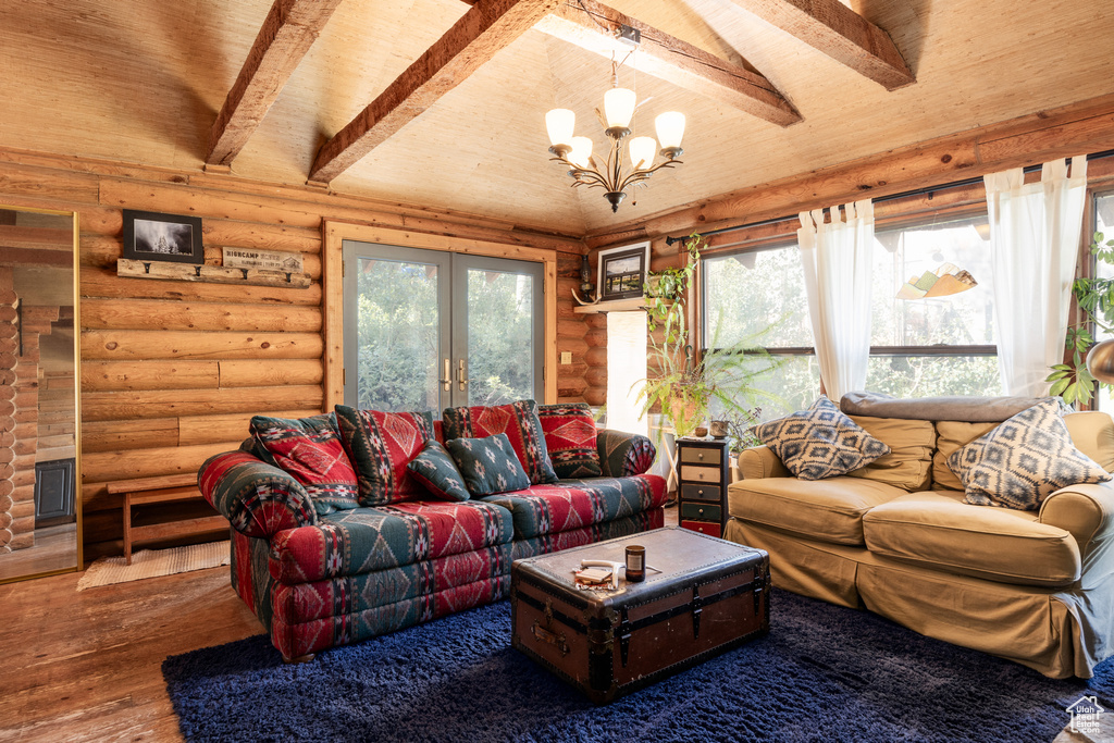 Living room with lofted ceiling with beams, french doors, rustic walls, wood-type flooring, and a notable chandelier