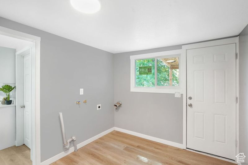 Laundry area with hookup for a washing machine, electric dryer hookup, and light hardwood / wood-style flooring