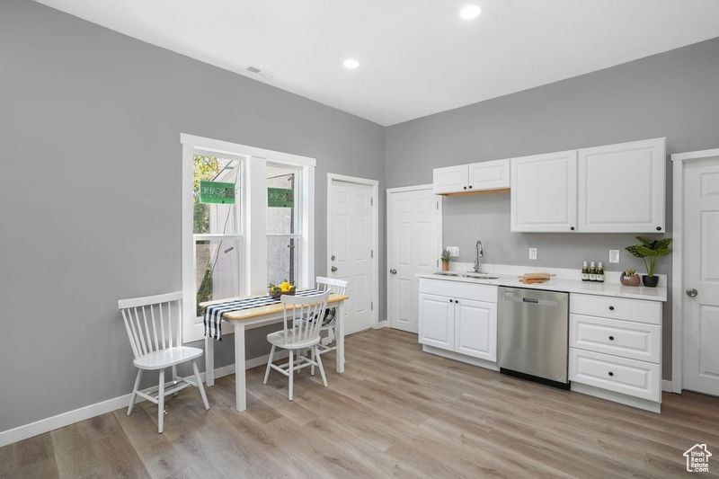 Kitchen featuring sink, stainless steel dishwasher, white cabinetry, and light hardwood / wood-style flooring