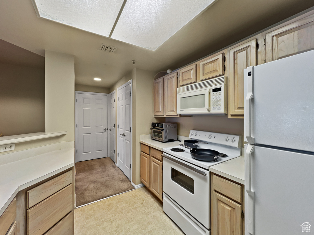 Kitchen with light tile patterned flooring, light brown cabinets, and white appliances