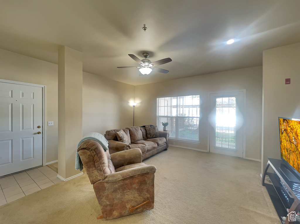 Living area with light carpet, ceiling fan, baseboards, and light tile patterned floors