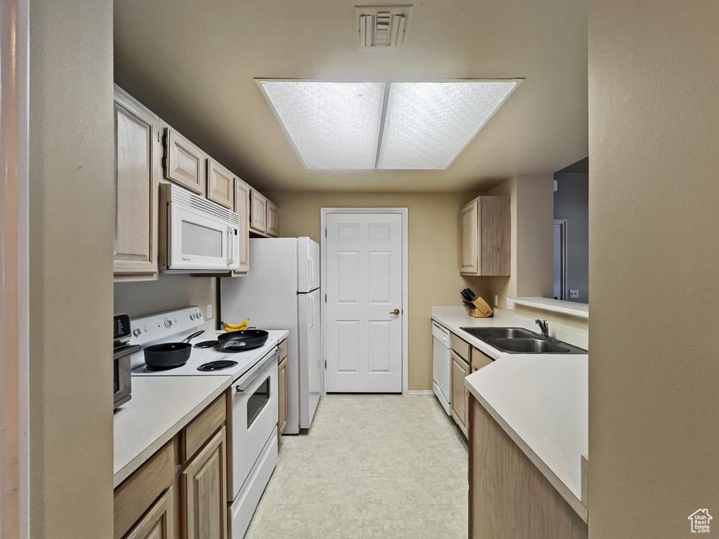 Kitchen featuring light tile patterned floors, light brown cabinets, white appliances, and sink