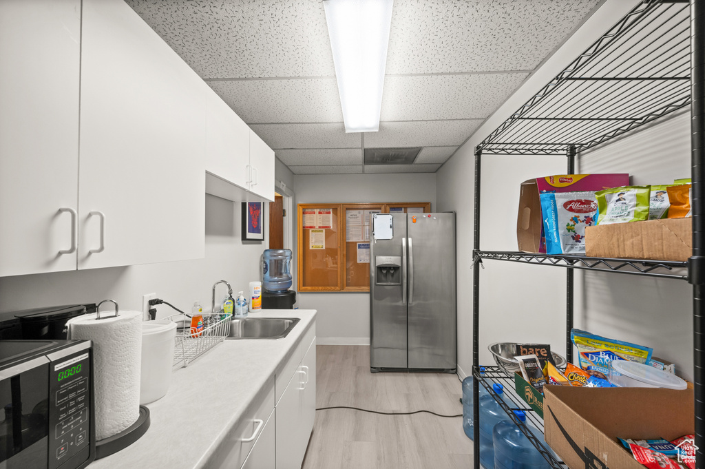 Kitchen with a paneled ceiling, light wood-type flooring, white cabinets, and stainless steel fridge